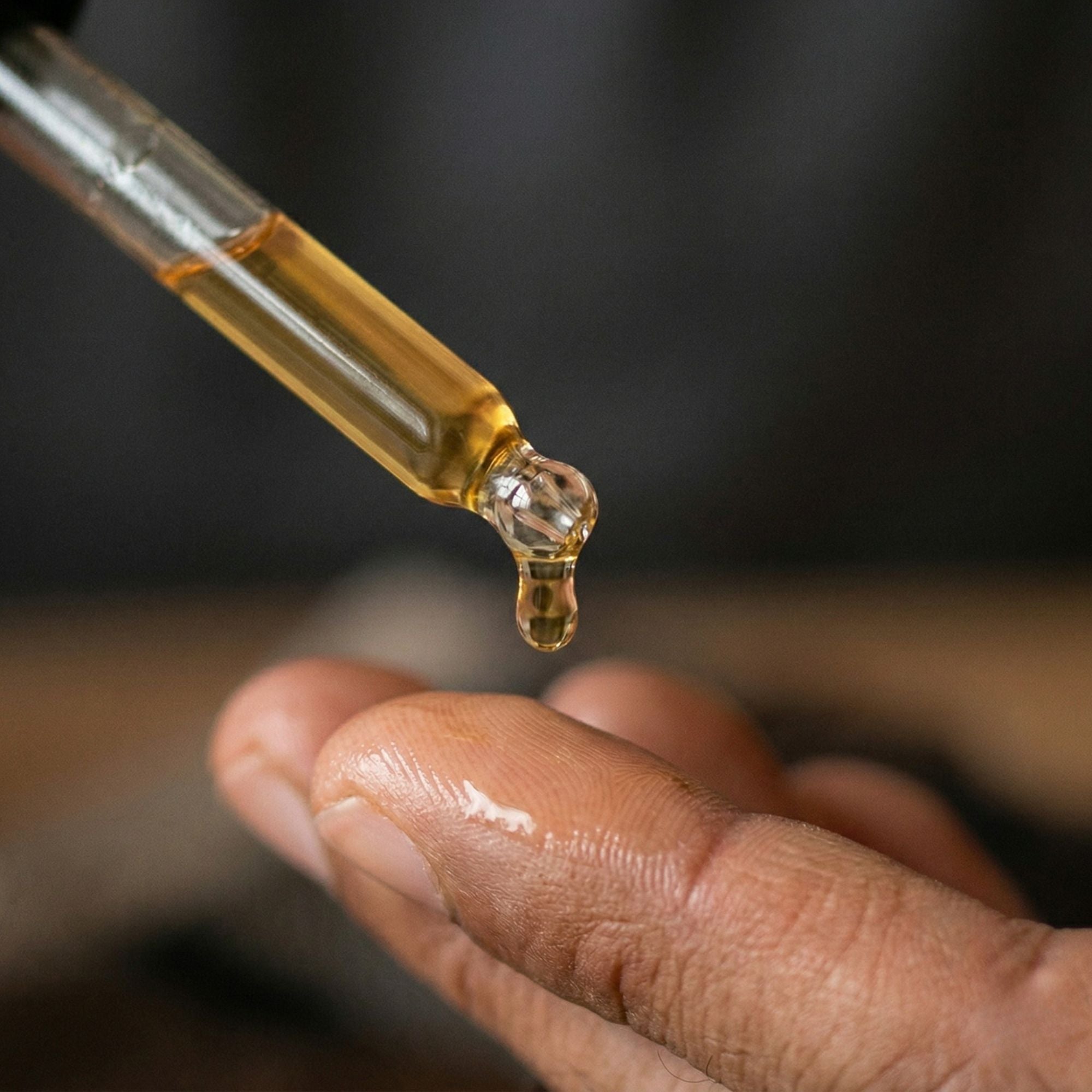Close-up of a dropper with a drop of liquid being placed on a person's palm.